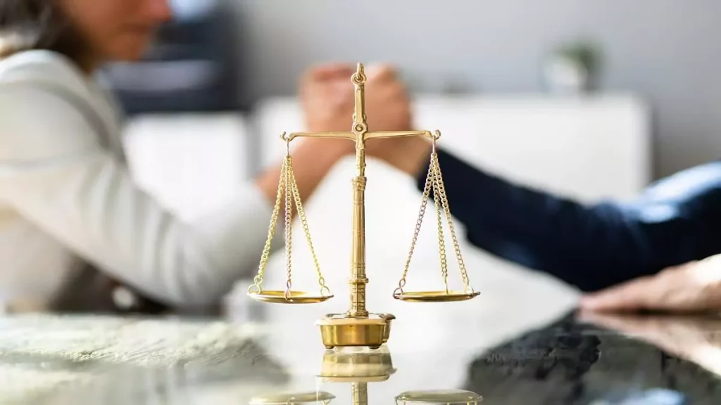Mulher e homem em queda de braço com balança da Justiça à frente